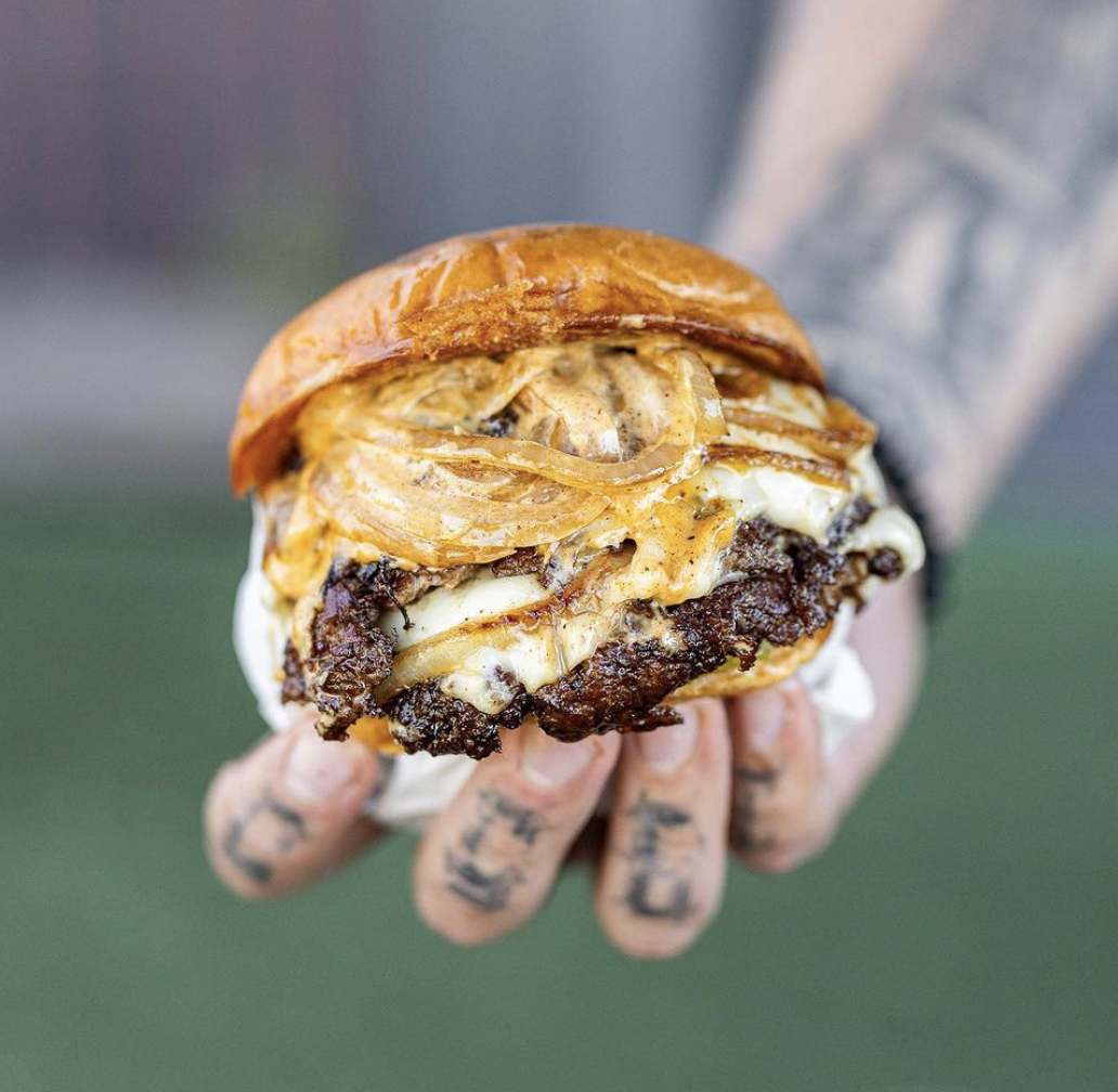photo of a burger held by a hand with tattoos on the person's fingers.